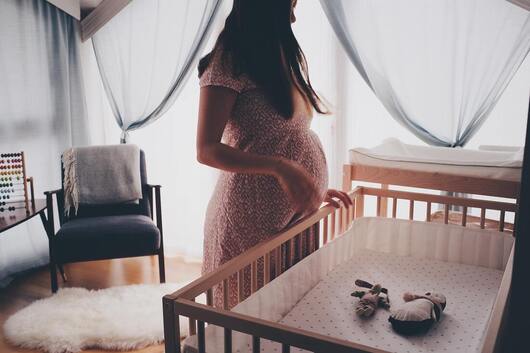 Pregnant mother standing beside an empty crib